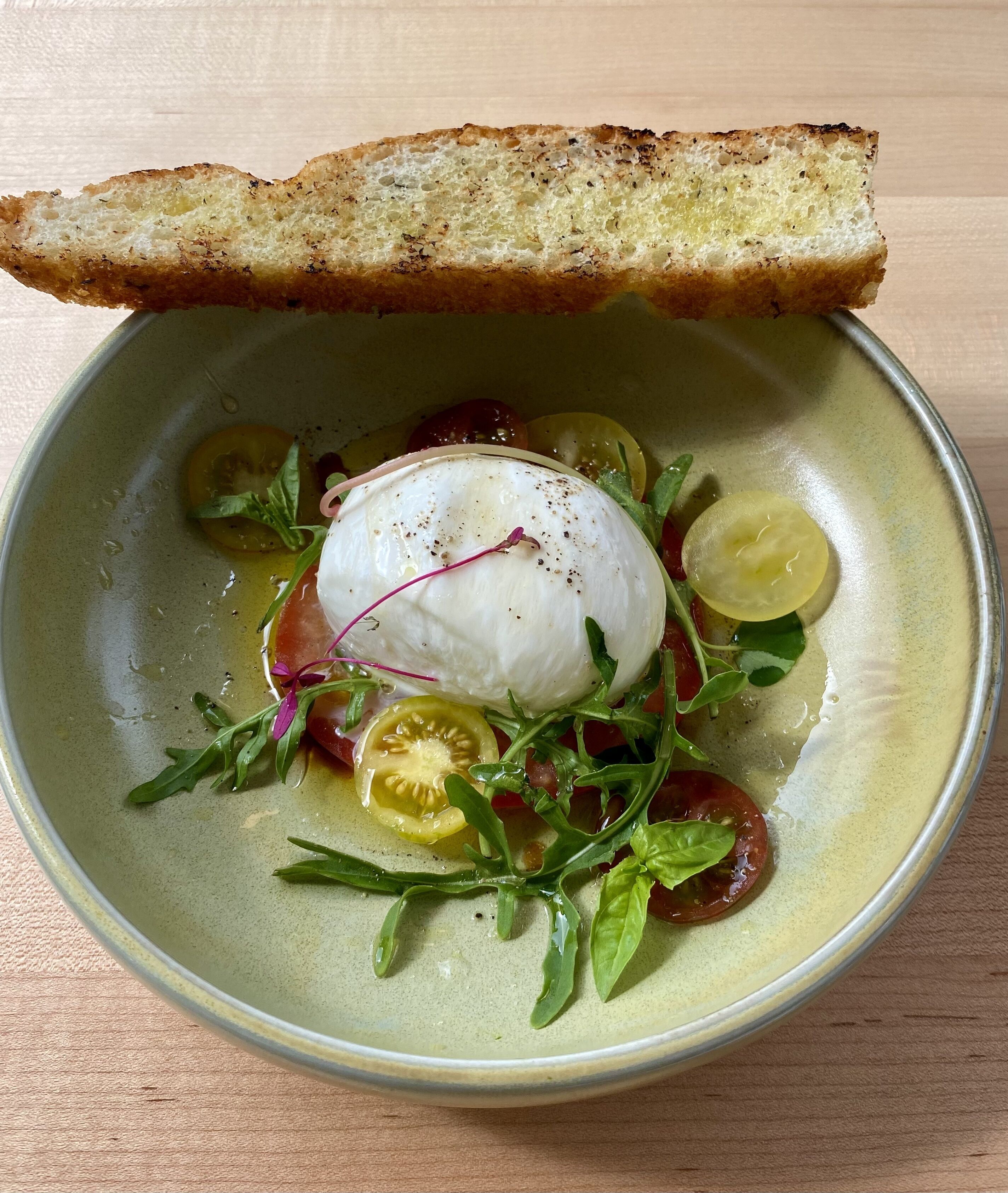 A bowl of food with a poached egg, tomatoes, and greens, accompanied by a slice of bread.