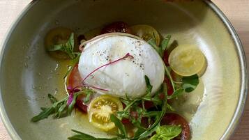 A bowl of food with a poached egg, tomatoes, and greens, accompanied by a slice of bread.