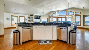 A spacious kitchen with a large island, white cabinets, and a view of the outdoors through large windows. - Sand Pebbles: Oceanfront, Pool, Hot Tub, Rec Room (Nags Head)