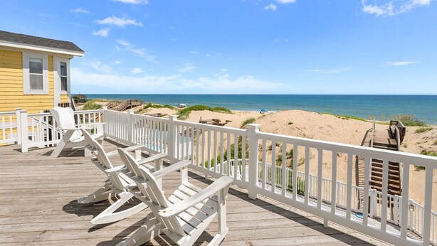 A wooden deck with white railings overlooking a beach. - Sand Pebbles: Oceanfront, Pool, Hot Tub, Rec Room (Nags Head)