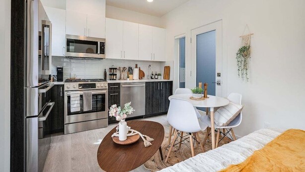 A modern kitchen with stainless steel appliances, white cabinetry, and a dining area with a wooden table and white chairs. - Perch - Urban Reflections 18: WS 97 | Cozy Home | Rooftop City View (Seattle)