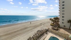 A beach view from a hotel balcony with a pool and a clear sky.
