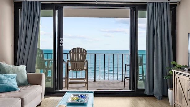A balcony with a view of the ocean, a wooden chair, a sofa, and a table with a tray.
