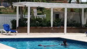 Une piscine agrémentée d’une pergola blanche et d’une chaise longue bleue.