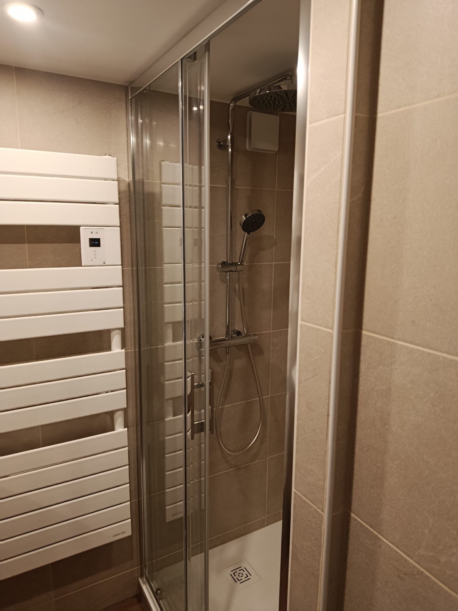 A modern bathroom with a glass-enclosed shower, a control panel, and a white towel rack.