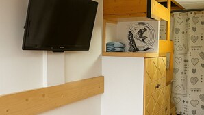 Une pièce avec un téléviseur fixé au mur, un banc en bois, un meuble orné d’un motif géométrique et un rideau à motifs.
