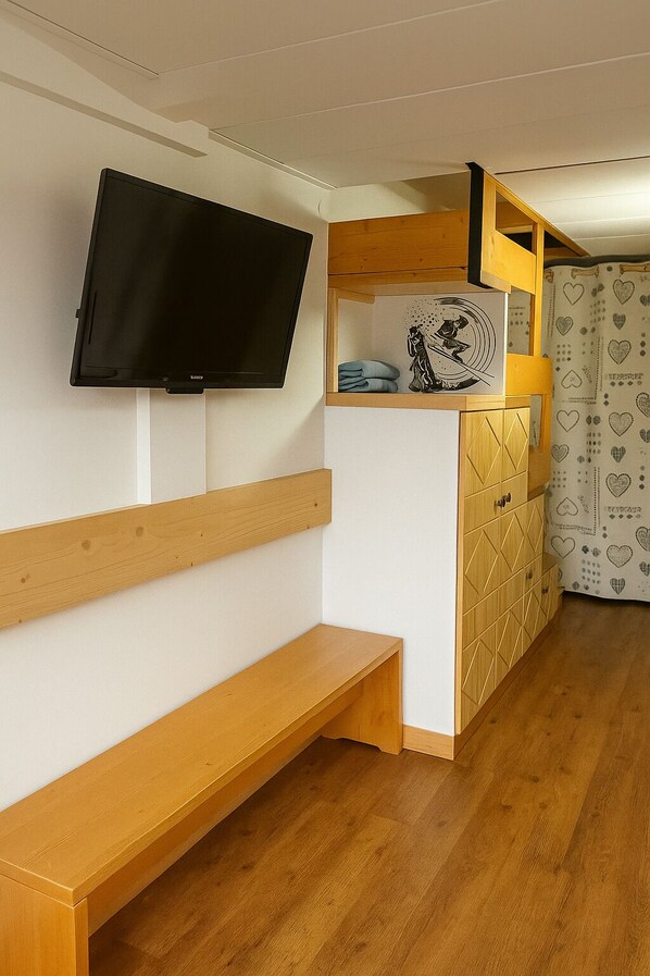 Una habitación con una televisión montada en la pared, un banco de madera, un mueble con un diseño geométrico y una cortina estampada.