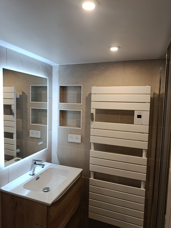 Un baño moderno con un espejo grande, un lavamanos blanco y un perchero empotrado.