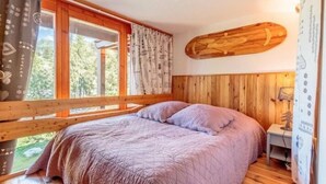 Une chambre à coucher avec un lit, des murs en bois, une fenêtre avec des rideaux et une poutre en bois au plafond.