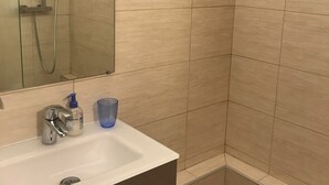 Une salle de bain avec une douche, un lavabo avec un miroir et une tasse bleue.
