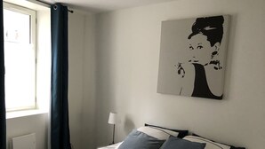 A bedroom with a bed, a window with curtains, a wall-mounted artwork, and bedside lamps. - Charming single-storey studio in a quiet location  (La Chapelle-Saint-Mesmin)