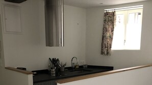 A compact kitchen with a built-in stove, a sink, and a window with floral curtains. - Charming single-storey studio in a quiet location  (La Chapelle-Saint-Mesmin)