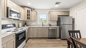 A modern kitchen with light wood cabinets, stainless steel appliances, a dishwasher, and a window providing natural light.