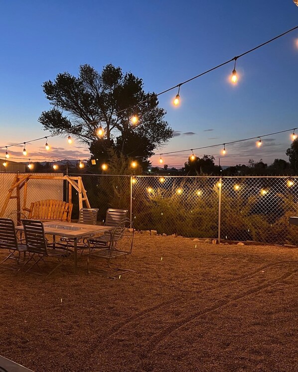 An outdoor patio area with a wooden table and chairs, surrounded by a chain-link fence.