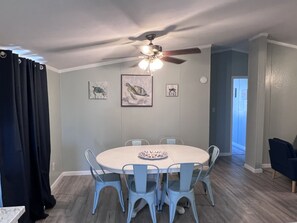A dining area with a round table, six chairs, ceiling fan, and artwork on the walls.