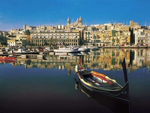 A harbor with boats docked, a calm water surface reflecting buildings, and a clear sky.