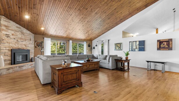 A spacious living room with a stone fireplace, wooden ceiling, and large windows.