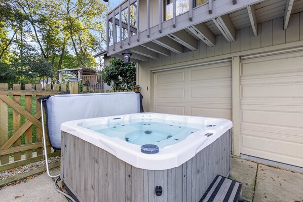 Un bain à remous dans un jardin, avec une terrasse en bois, un garage et une clôture en bois.
