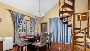 A dining area with a table, chairs, a chandelier, and a wooden spiral staircase.