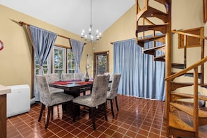 A dining area with a table, chairs, a chandelier, and a wooden spiral staircase.