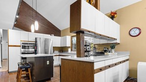 A modern kitchen with white cabinetry, a stainless steel refrigerator, a wooden island, and a clock on the wall.