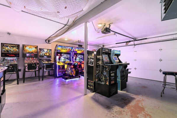 A room with arcade games, a large screen, and a ceiling-mounted projector.