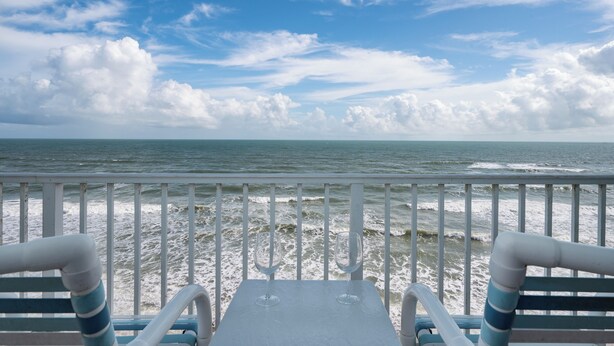 Une vue depuis un balcon donnant sur l’océan, où l’on peut voir les vagues se briser sur le rivage.