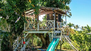 Un parque infantil tipo casa del árbol con tobogán, estructuras para escalar y una plataforma de madera.