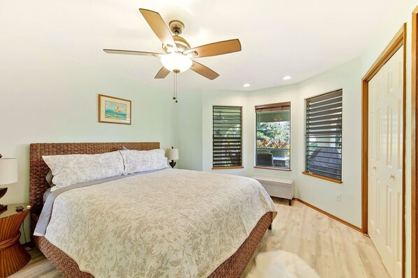 A bedroom with a large bed, a ceiling fan, a nightstand, a lamp, and a window with blinds. - Sunny Family Oasis ☀ Tree House, Trampoline, Games, Toys (Princeville)