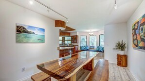 Una cocina moderna con una isla de madera alargada, un comedor con banco y vistas al océano a través de amplios ventanales.