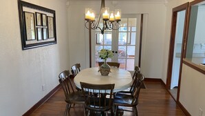 A dining room with a round table, six chairs, a chandelier, and framed botanical prints on the wall. - Dewey Cottage - Central to All of SEMO Adventures (Farmington)