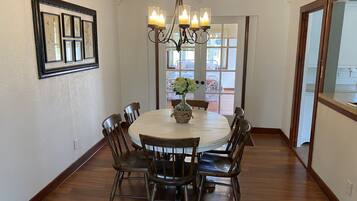 A dining room with a round table, six chairs, a chandelier, and framed botanical prints on the wall.