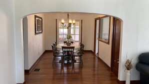 A dining area with a round table, chairs, a chandelier, and a window with a view. - Dewey Cottage - Central to All of SEMO Adventures (Farmington)