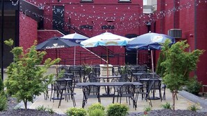 An outdoor patio with tables and umbrellas, surrounded by a garden with small trees and shrubs. - Dewey Cottage - Central to All of SEMO Adventures (Farmington)
