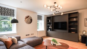 Una sala de estar moderna con un sofá modular, una mesa de centro con una planta, un televisor de pantalla plana grande y estanterías empotradas.