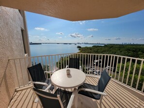 A balcony with a table and chairs, overlooking a body of water and a distant city skyline. - Lovers Key Resort Suite 5 - Bay View (Bonita Springs)