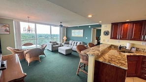 A spacious living area with a large window, a kitchen with wooden cabinets, and a dining area with wicker furniture. - Lovers Key Resort Suite 5 - Bay View (Bonita Springs)