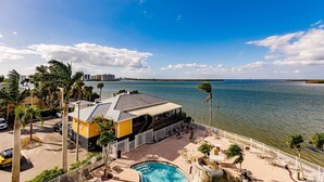 A waterfront hotel with a pool, outdoor seating, and a view of the sea and distant buildings. - Lovers Key Resort Suite 5 - Bay View (Bonita Springs)