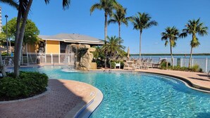 A swimming pool with lounge chairs, palm trees, and a building with a waterfall feature. - Lovers Key Resort Suite 5 - Bay View (Bonita Springs)