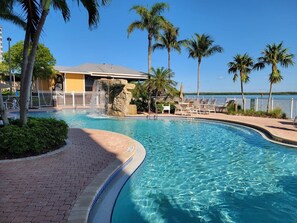 A swimming pool with lounge chairs, palm trees, and a building with a waterfall feature. - Lovers Key Resort Suite 5 - Bay View (Bonita Springs)