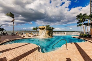 A swimming pool with a rock feature, surrounded by lounge chairs and palm trees. - Lovers Key Resort Suite 5 - Bay View (Bonita Springs)