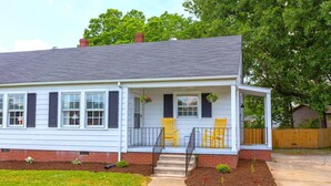 A single-story house with a covered porch, a brick foundation, and a well-maintained lawn. - Charming parkview from rocking chair front porch (Graham)