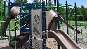 A playground with a slide, climbing structures, and a covered area. - Charming parkview from rocking chair front porch (Graham)