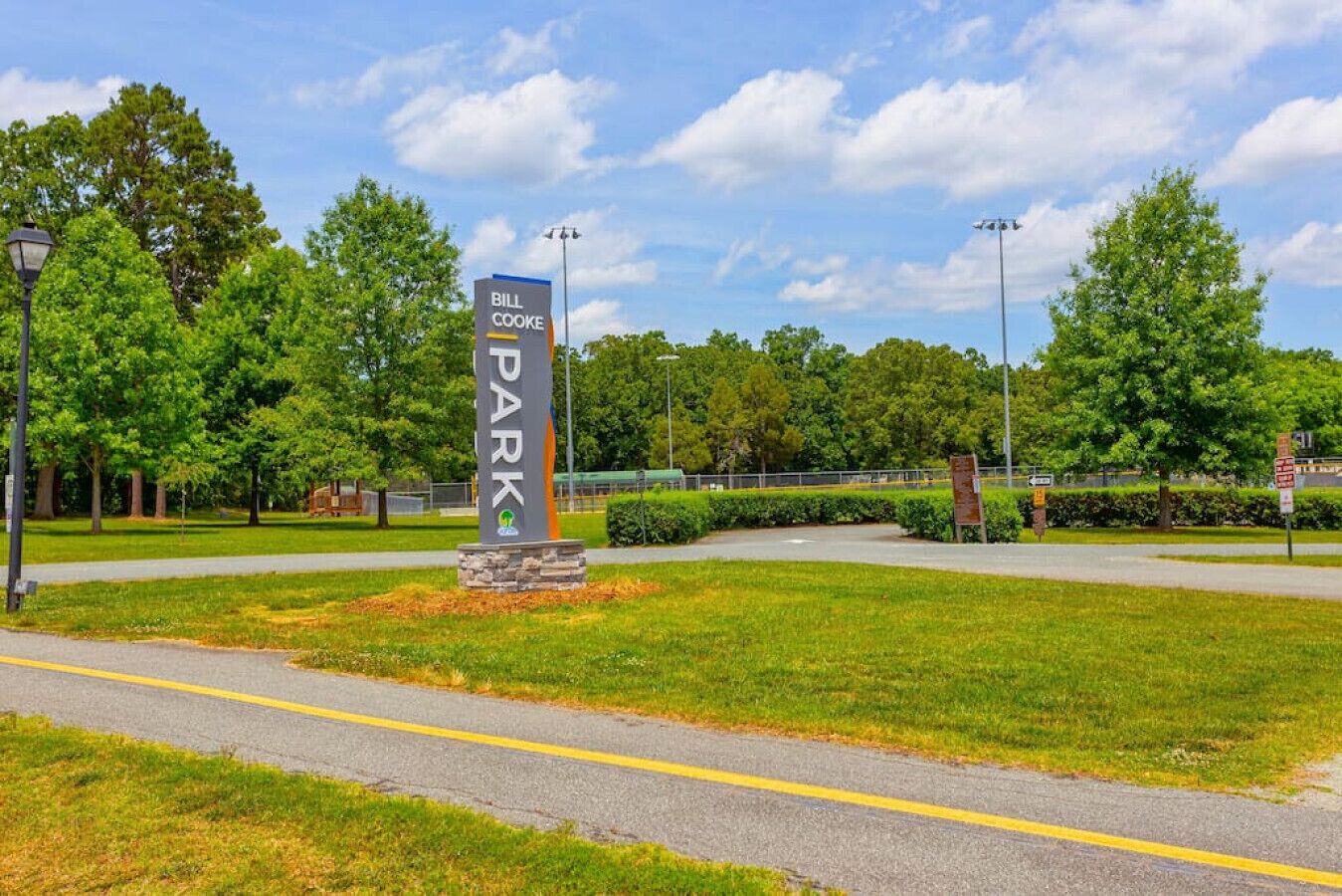 A sign for Bill Cooke Park with a clear sky and trees in the background.