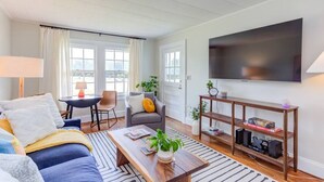 Una sala de estar moderna con un sofá, una mesa de centro, televisor y una mesita con lámpara y libros.