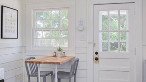 Una habitación con una mesa de madera y dos sillas, una puerta blanca y una ventana con vistas a árboles.