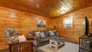 A cozy wooden cabin interior with a sofa, armchair, coffee table, and a television. - Pine Ridge Cabin: an all-seasons Wellsboro getaway (Charleston Township)