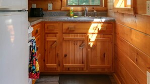 A compact kitchen with wooden cabinets, a white refrigerator, a sink, and a window providing natural light. - Pine Ridge Cabin: an all-seasons Wellsboro getaway (Charleston Township)