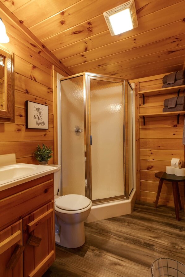 Une salle de bain en bois avec une douche à parois de verre, des toilettes, un lavabo et une petite table avec des serviettes.