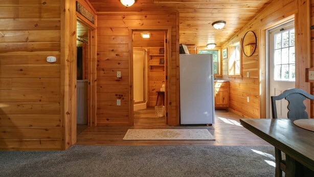 A wooden cabin interior with a kitchen area, a dining table, and a refrigerator. - Pine Ridge Cabin: an all-seasons Wellsboro getaway (Charleston Township)